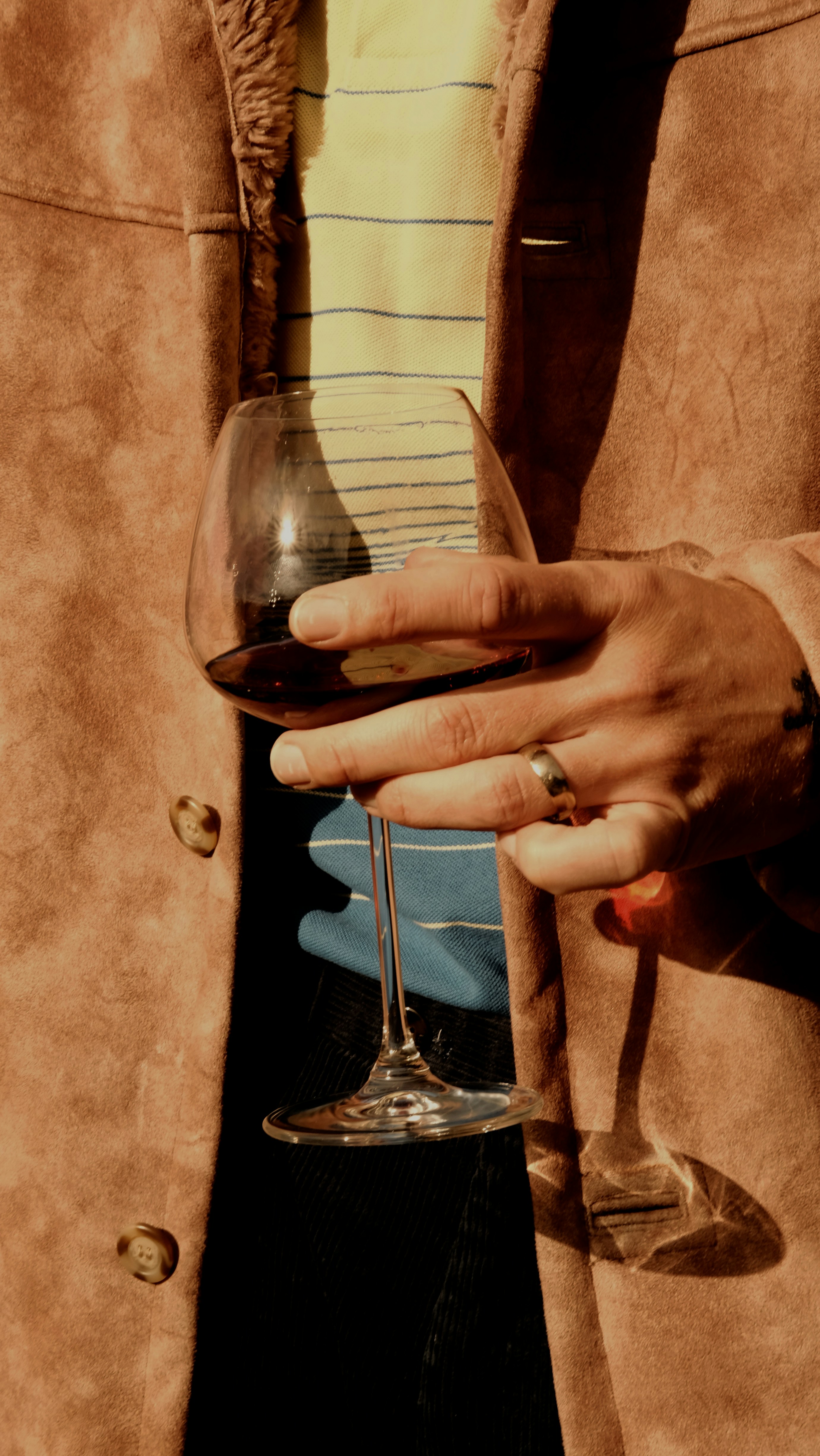 Person hält ein Glas Rotwein im Sonnenlicht